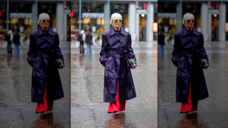 Grece Ghanem walking wearing a long purple snakeskin jacket and green sunglasses
