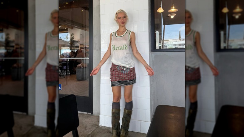 Iris Law smiles wearing a white tank top and a tartan skirt