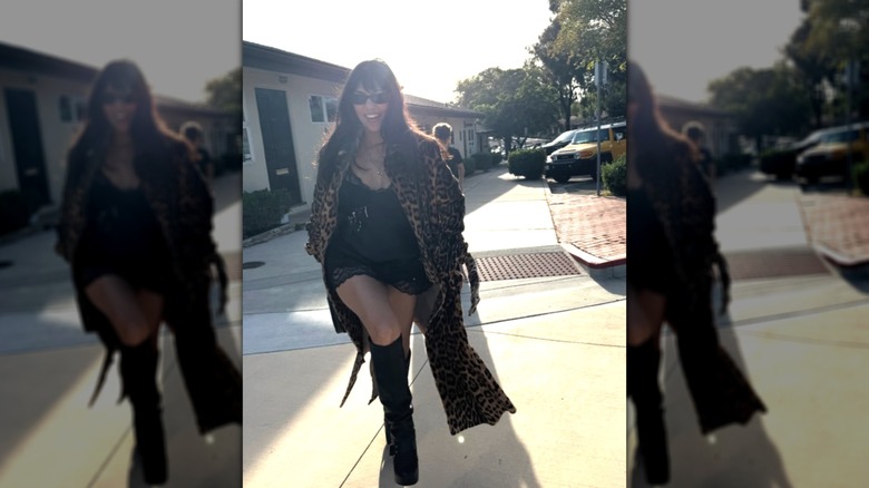 Kourtney Kardashian Barker walking wearing a black slip dress and a leopard-print coat