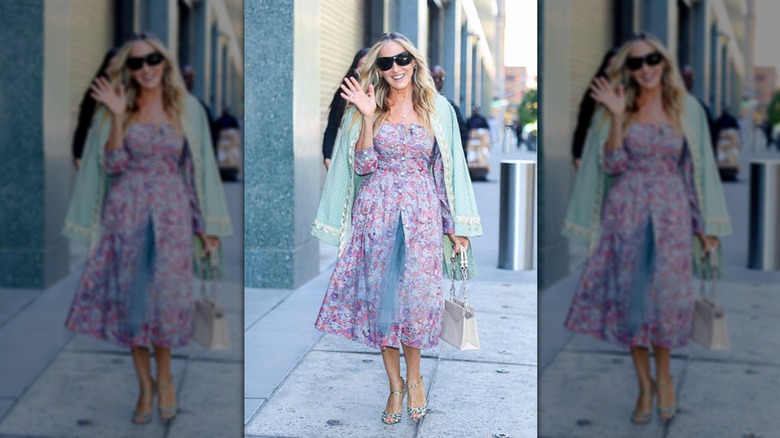 Sarah Jessica Parker smiles and waves wearing a floral dress and sunglasses