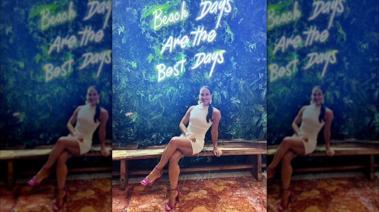 Emily Compagno in a white dress posing in front of a green background with a neon sign