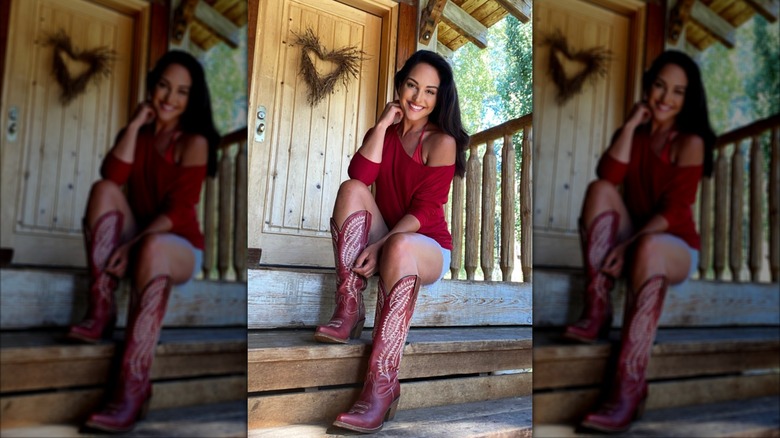 Emily Compagno sitting on a front porch in a red top, denim shorts and red cowboy boots