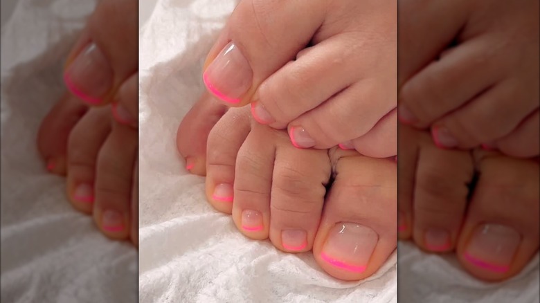 A close-up of a classic French pedicure with a pop of colored tip by Milly Mason