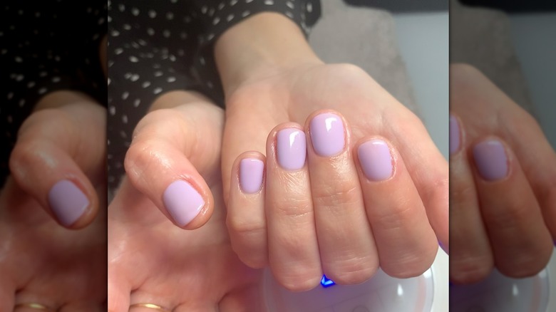 A woman showing a milky lavender manicure on short nails