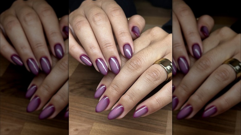 Hands resting on a table with an aura purple manicure