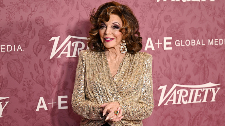 Joan Collins in a gold top and big earrings at an event in June 2026
