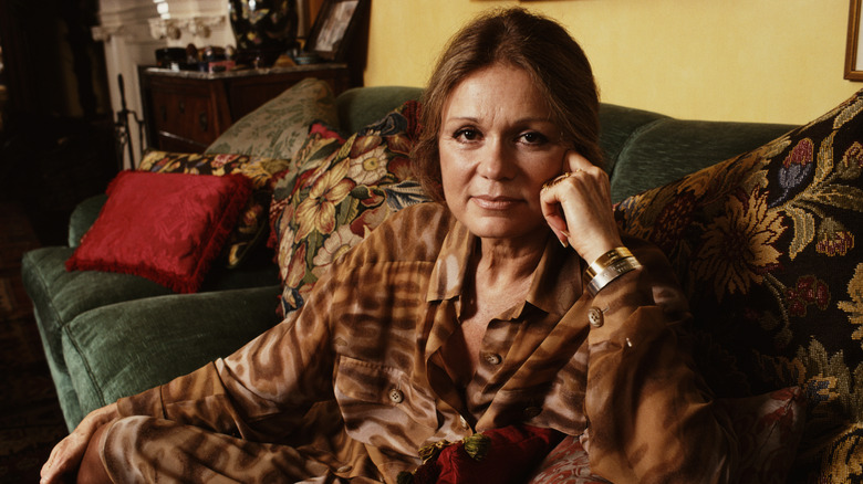 Gloria Steinem sat on green sofa in brown blouse