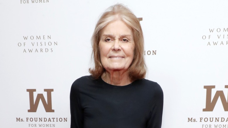 Gloria Steinem posing on the red carpet in front of a white background