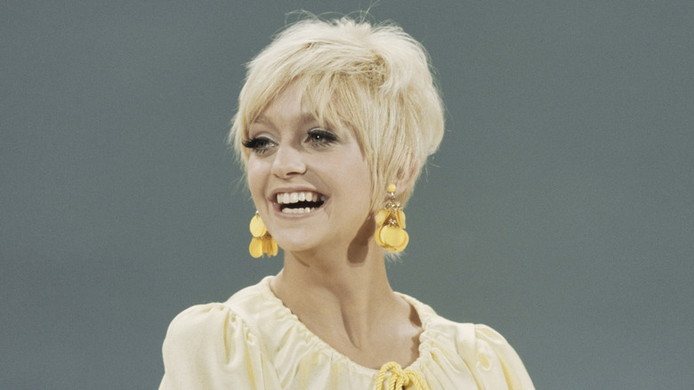 Goldie Hawn grinning on a 1960s TV show with yellow earrings and short hair.