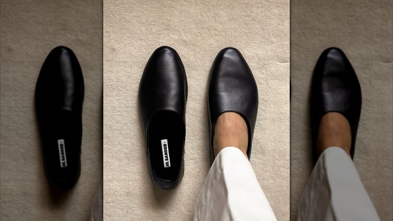 Two high-vamp black ballet flats and one has a foot in it
