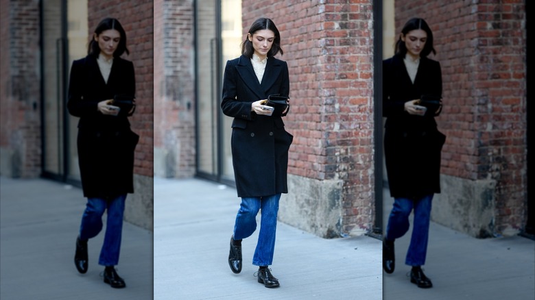 A woman walking on the street wearing a coat, blue jeans, and derby shoes