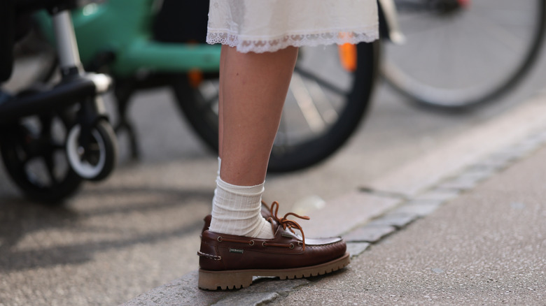 A woman standing on the street wearing a skirt and boat shoes
