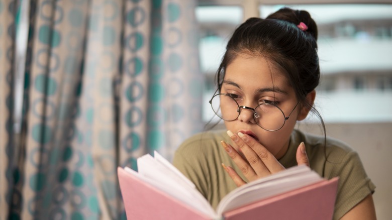 A young woman looking shocked while reading a book