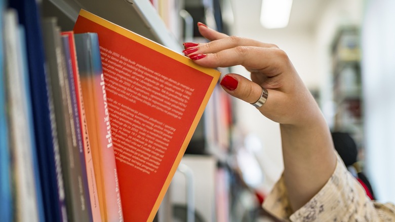A woman's hand with red nails taking a book off a shelf