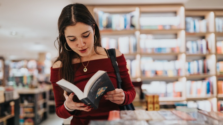 A woman with dark hair reading a book in a book store
