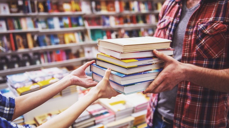 A person handing over a stack of books to another person in a book store