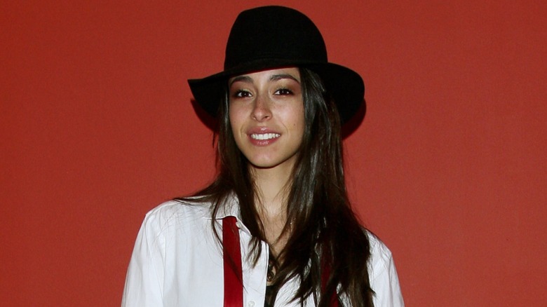 Oona Chaplin posing in a black hat and white shirt in front of a red background in 2010