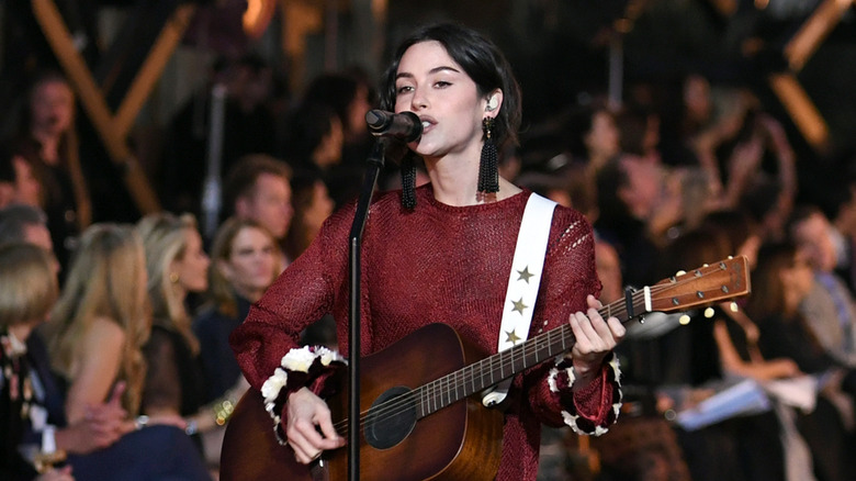 Gracie Abrams singing into mic while playing guitar