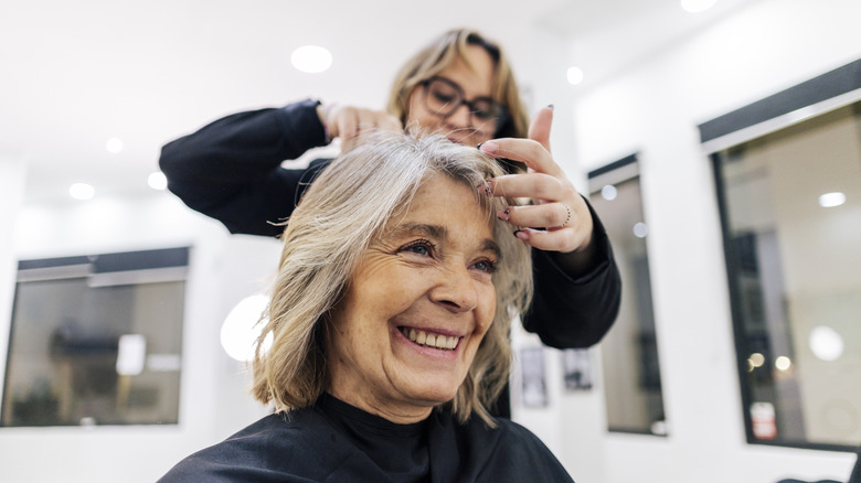 Woman sitting in salon chair with hairstylist styling her hair
