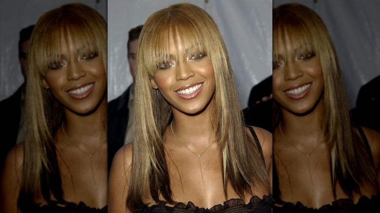 Beyoncé smiling on the red carpet with long, straight hair and bangs