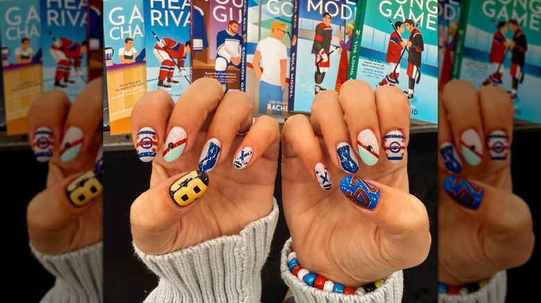 Hands with a "Heated Rivalry" manicure with the book series in the background