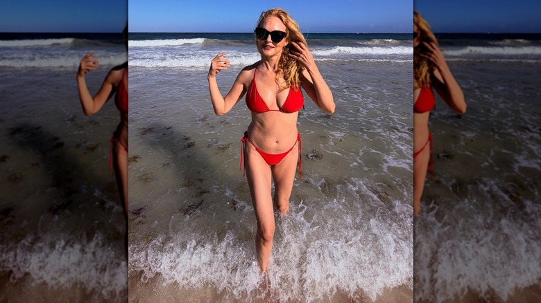 Heather Graham walking in shallow waves while wearing a red bikini and sunglasses