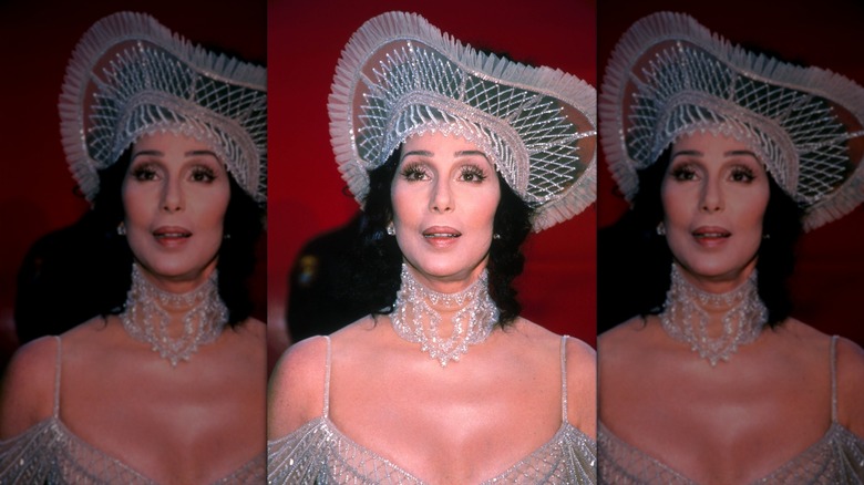 Cher on the red carpet in a large hat and sparkly dress in 1998