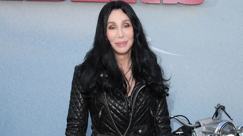 Cher smiling and posing next to a motorcycle in a black jacket in 2024