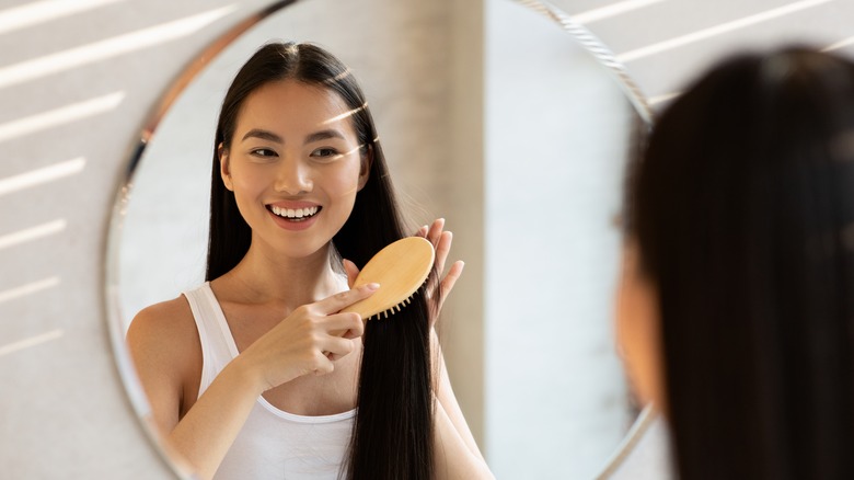 Woman brushing long hair mirror smiling