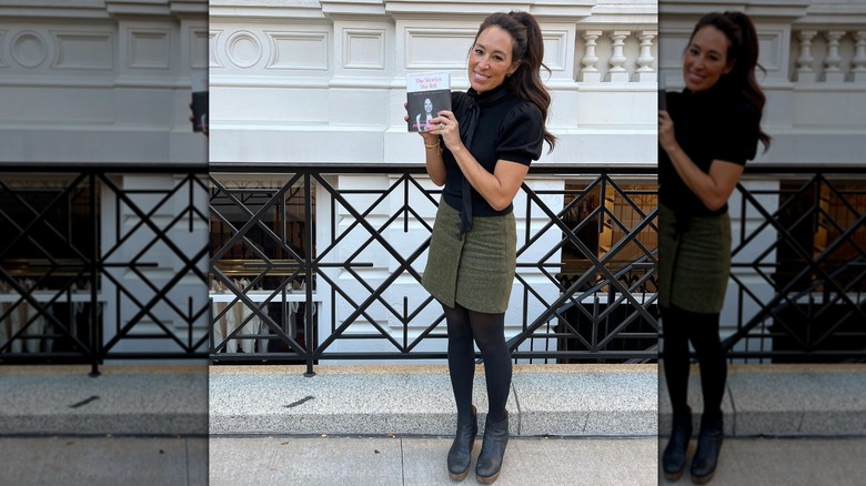Joanna Gaines posing on the sidewalk while holding up her book