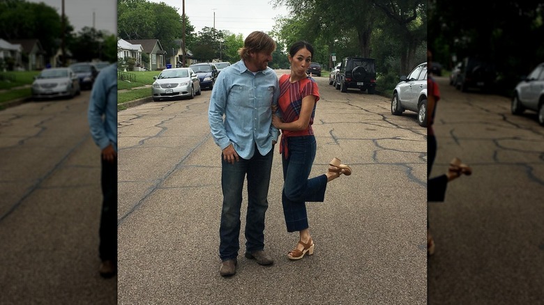 Joanna Gaines posing with husband Chip while making a silly face and kicking up one foot