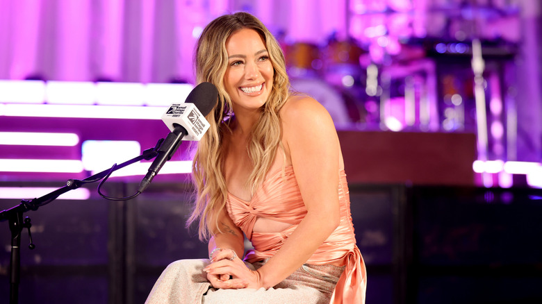 Hilary Duff sitting in front of a microphone in a pink top