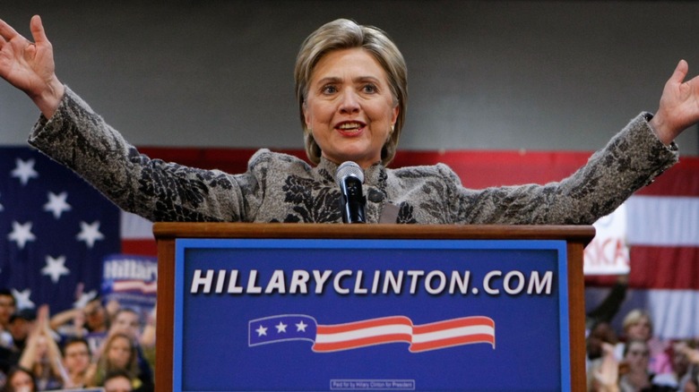 Hillary Clinton standing behind a podium with her arms outstretched.