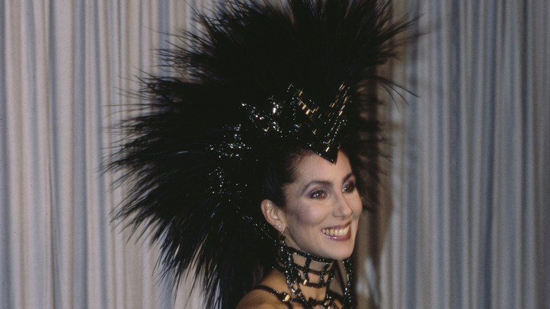 Cher smiles wearing a black spiked mullet wig