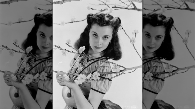 Vivien Leigh smiles behind a blossom tree with victory rolls.