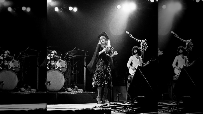 Stevie Nicks performing onstage with a tambourine in a top hat and platform boots