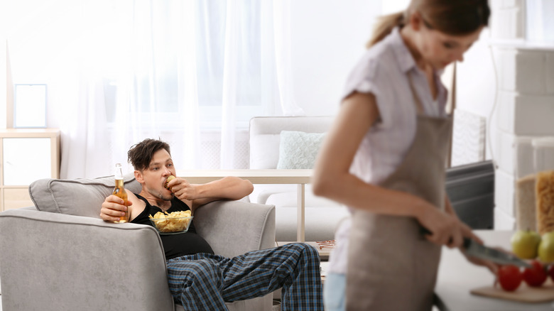 woman cooking while boyfriend lounges