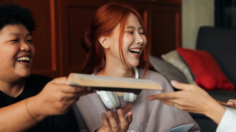 A group of friends smiling and laughing as they pass around a book