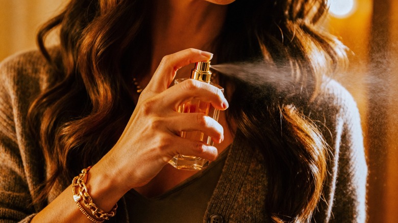 A woman spraying hair perfume onto her brunette, wavy, long hair
