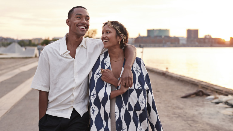 A couple walking and the man has his arm over his partner's shoulder