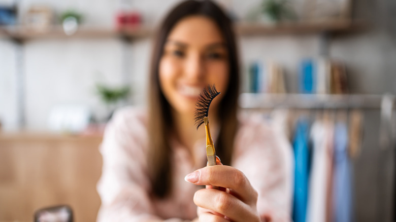 A woman holding some false eyelashes in a set of tweezers