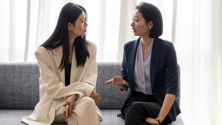 Two women in suits sitting on a couch and talking