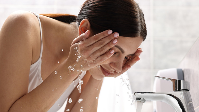 Woman washing face over sink