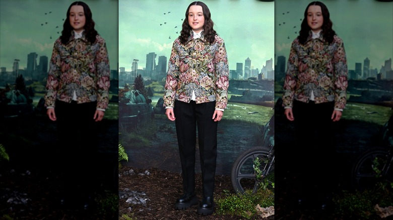 Bella Ramsey posing in a floral jacket and black chelsea boots at a show premiere