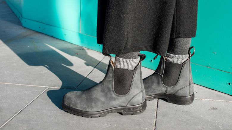 Close-up of grey, suede chelsea boots on pavement and next to turqouise wall