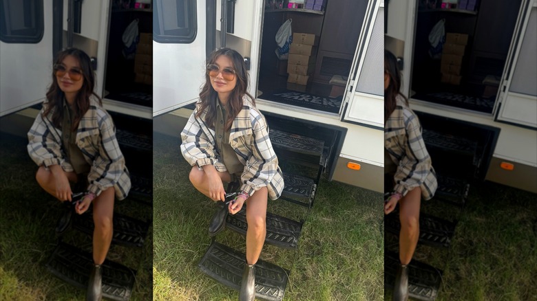 Gemma Chan sitting on RV steps while wearing a flannel shirt and chelsea boots