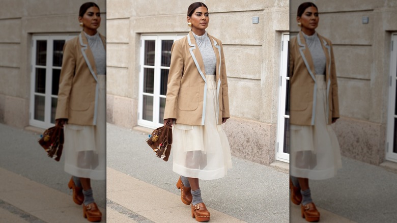 Zufi Alexander wears white sheer skirt, grey socks, brown mules, grey top, brown jacket and a brown suede bag with charms during Copenhagen Fashion Week