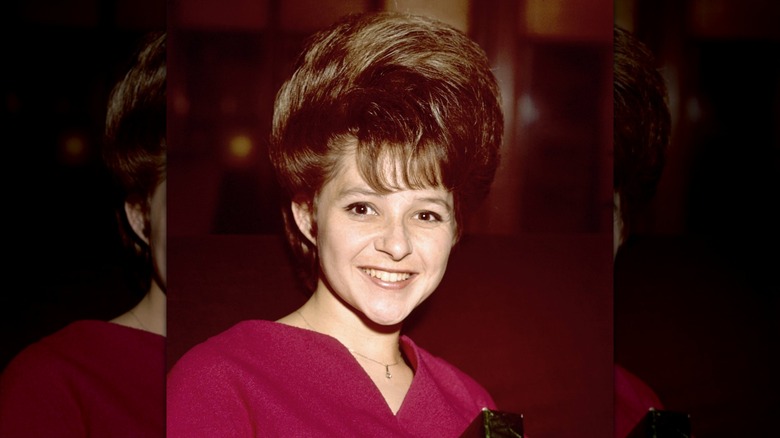 Brenda Lee smiles wearing a red dress and a bouffant combover
