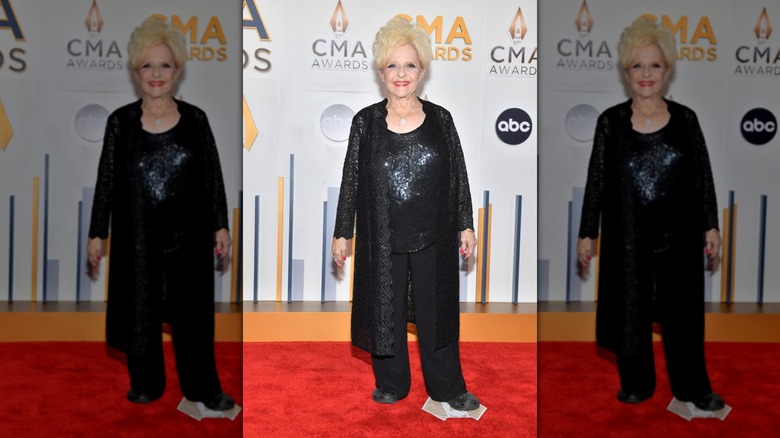 Brenda Lee smiles wearing a long black cardigan and a shiny black blouse