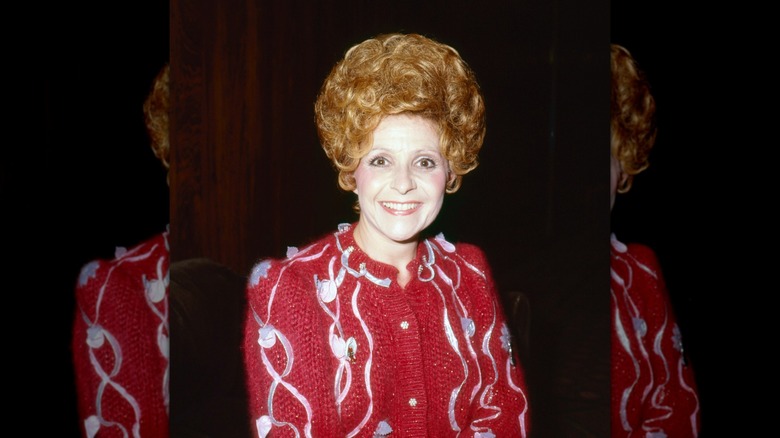 Brenda Lee smiles with ginger hair wearing a red cardigan